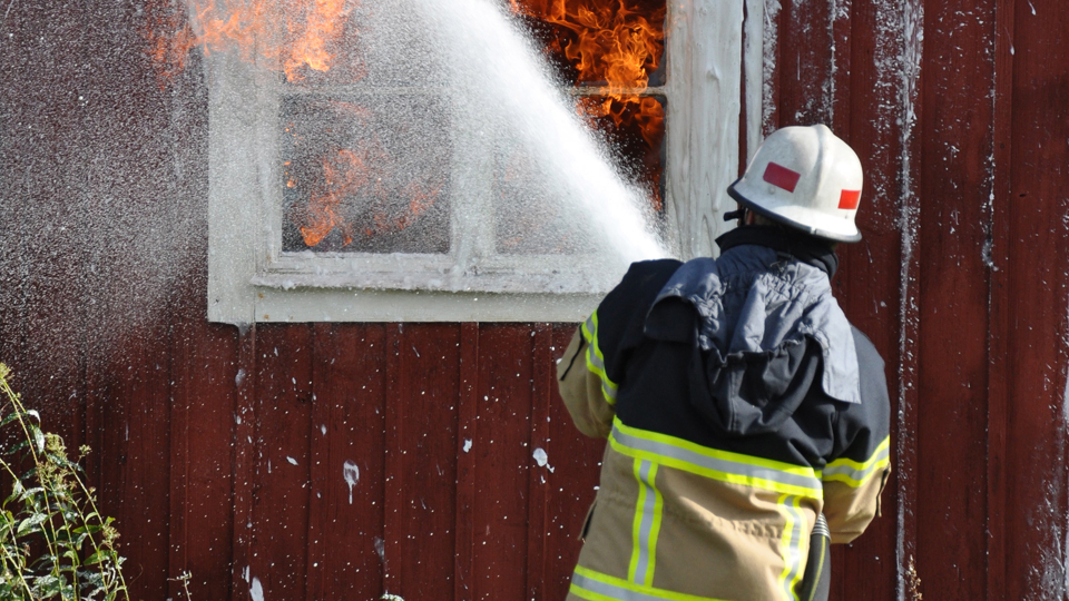 Brandman sprutar vatten på brinnande hus